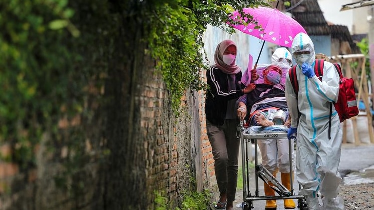 A woman holds a pink umbrella over a man on a stretcher, and they're accompanied by two medics.