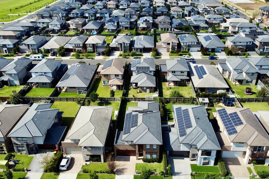 Bird's eye view of rows of newly built houses with green lawns and solar panels on roofs.