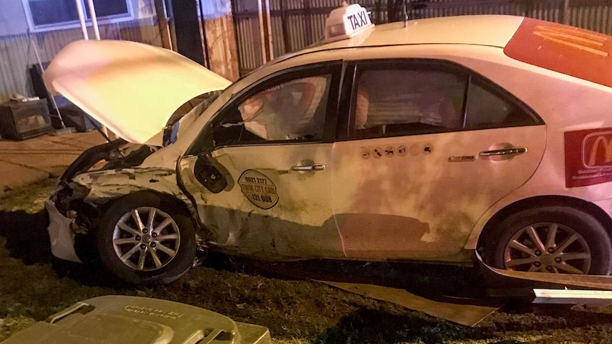 Night shot of a badly damaged taxi involved in a crash, in the front yard of a house.