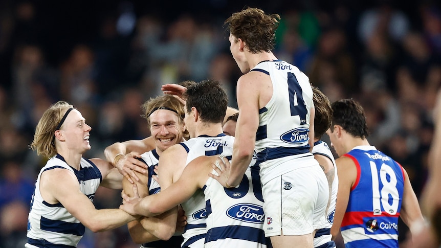 A group of Geelong AFL players celebrate a goal in a vital game.