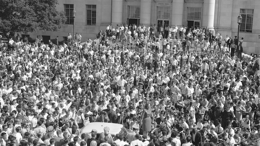 Black and white image of Jackie Goldberg giving a speech on a car surrounded by thousands of students activists