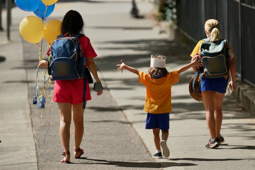 Parent holding balloons walks with two primary school children after school in Brisbane