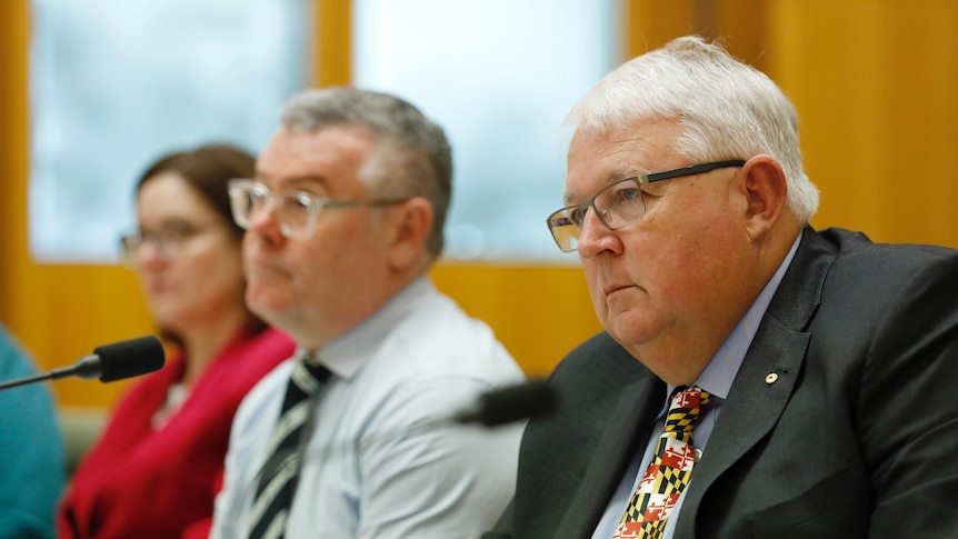 Andrew Metcalfe sitting behind a microphone at a desk in focus, murray watt next to him out of focus