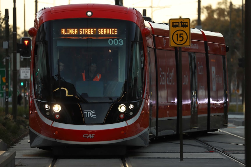 Light rail vehicles drive along a track at sunset.