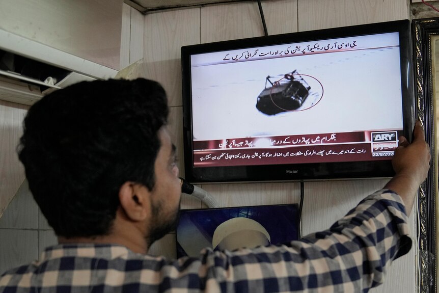 A man watches a news channel airing news regarding people trapped in a cable car.
