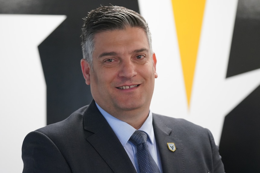 An older man in a suit and tie, smiling.