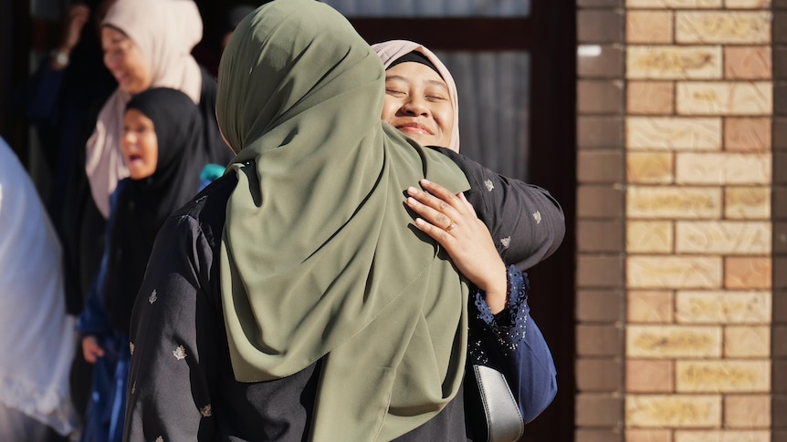 Two Muslim women hug outside a Mosque.