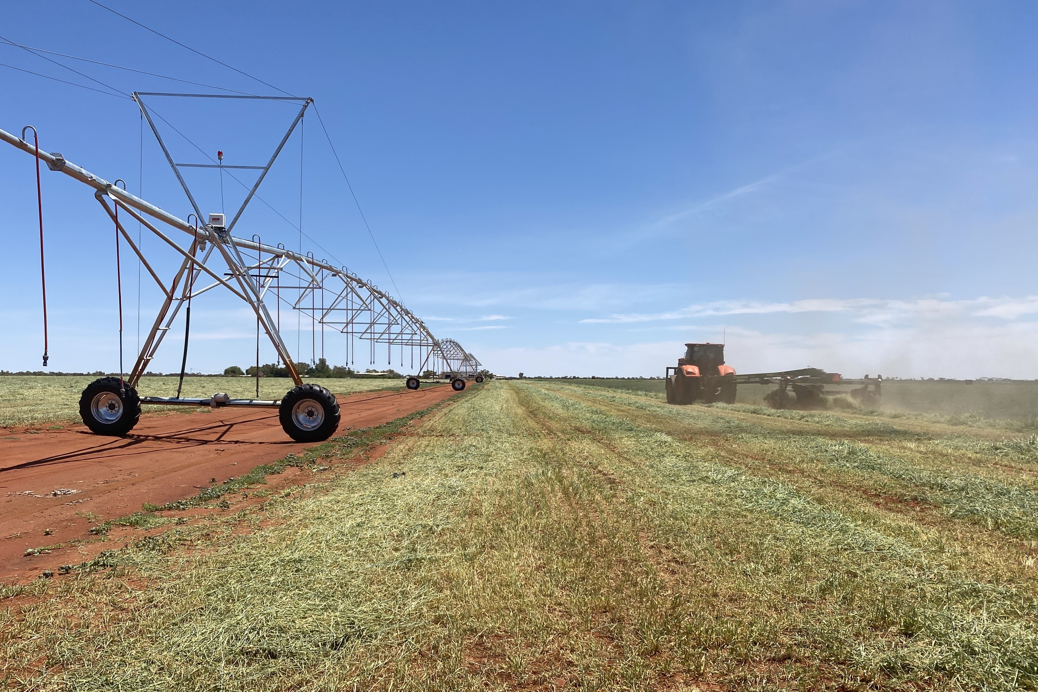 Um trator colhendo cevada, com um grande sistema de irrigação à esquerda.