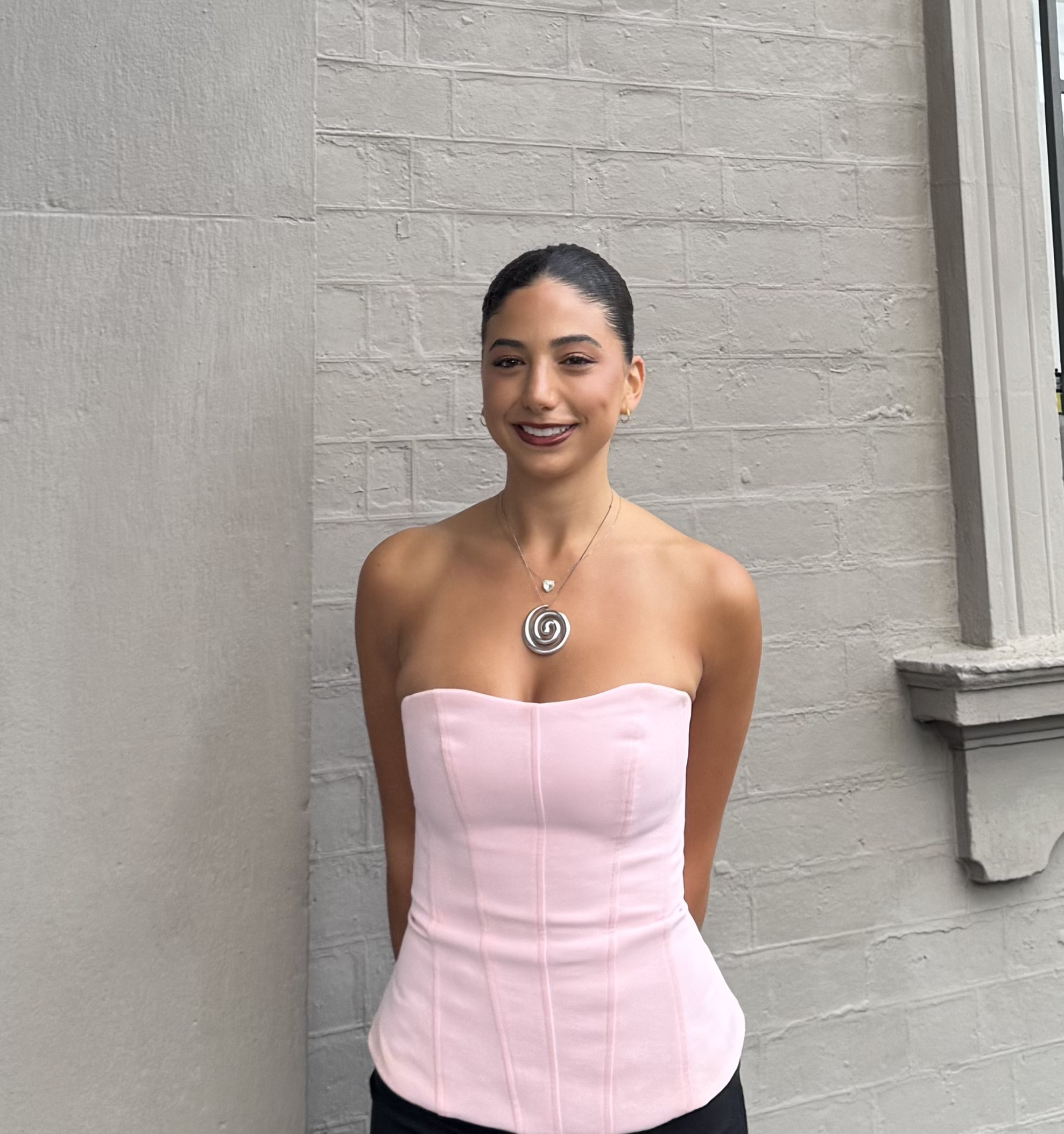 Uma garota com um rabo de cavalo escuro e uma blusa rosa claro.