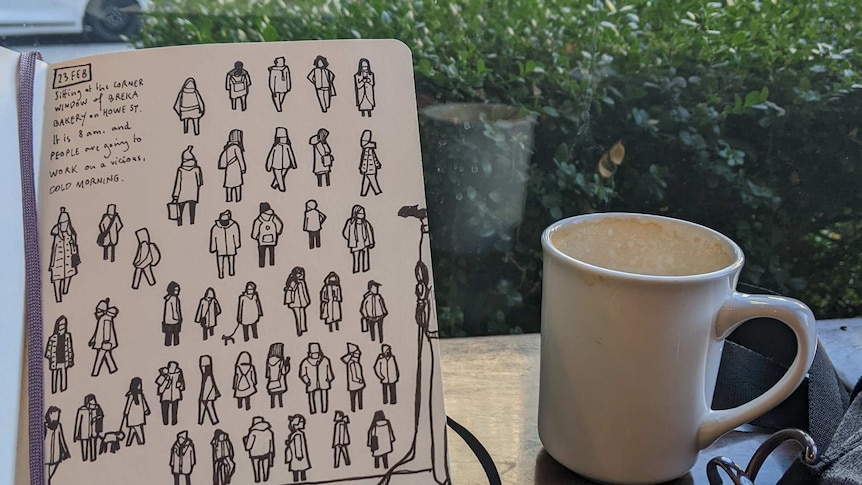 Sketchpad with line drawings of people on a table next to an empty white mug.