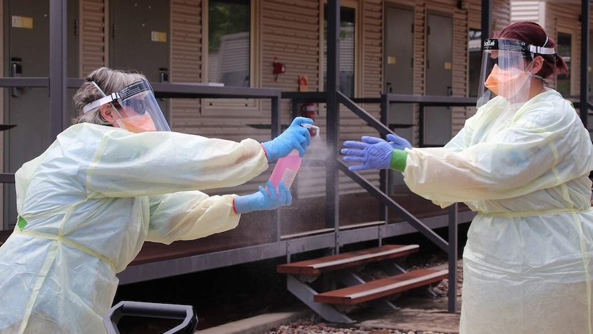 Two health workers in full PPE spray sanitiser on each other's hands. They are at Howard Springs quarantine facility.
