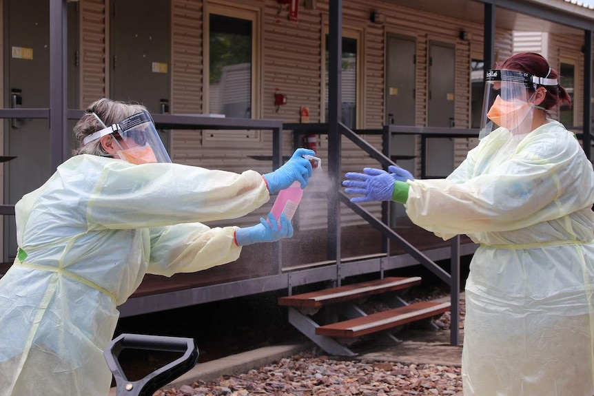 Two health workers in full PPE spray sanitiser on each other's hands. They are at Howard Springs quarantine facility.