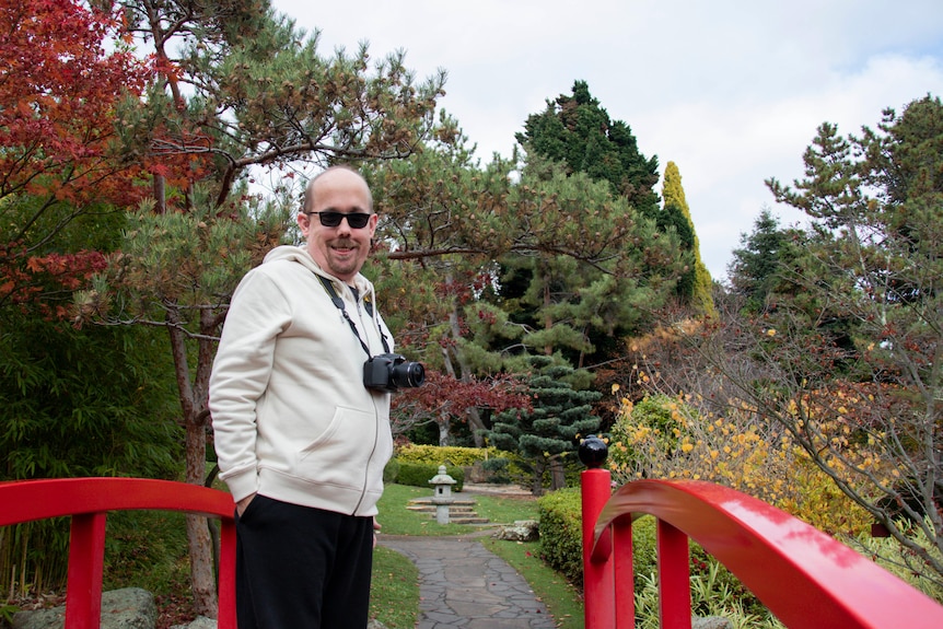 A man stands with a camera around his neck stands on a bridge