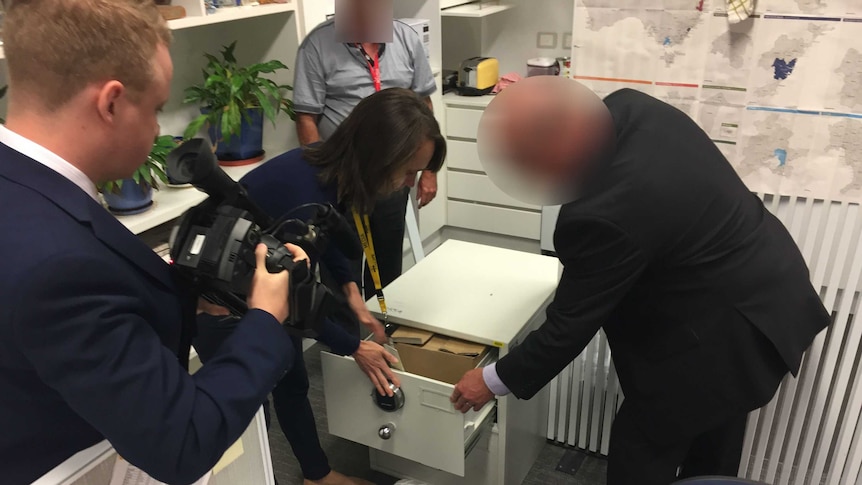 Files are locked away in a white safe. ASIO staff are present, and their faces are blacked out for legal reasons.