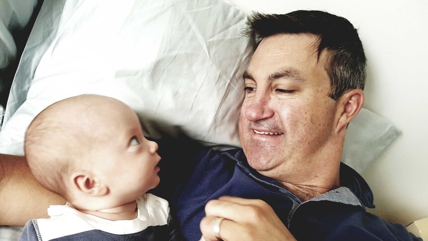 A baby looks up at his father while lying in bed