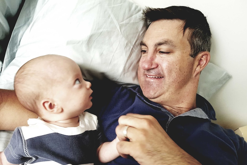 A baby looks up at his father while lying in bed