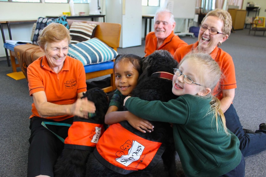 Students sit with volunteers and the dogs that help them read.