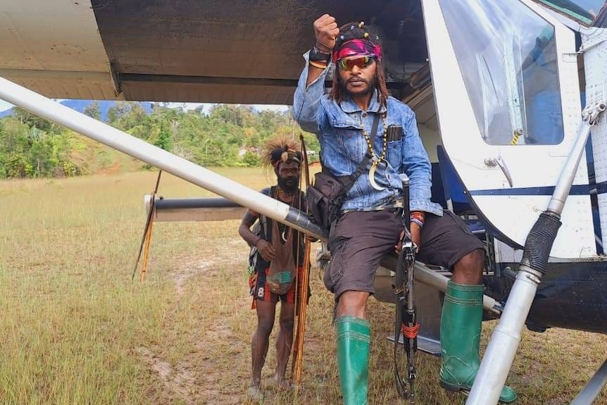 A man with a rifle raises his fist as he sits on a small aircraft.