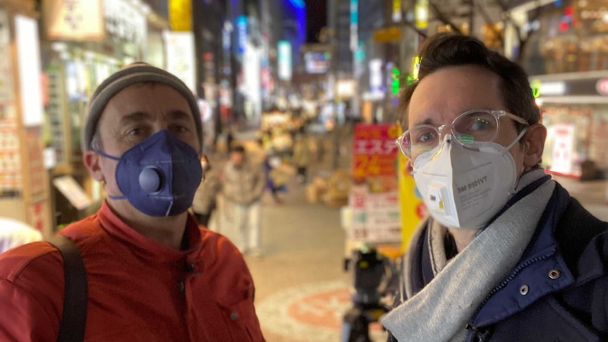 Bill Birtles and Brant Cumming in face masks standing on a Korean street at night