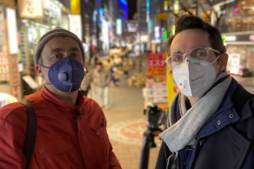Bill Birtles and Brant Cumming in face masks standing on a Korean street at night