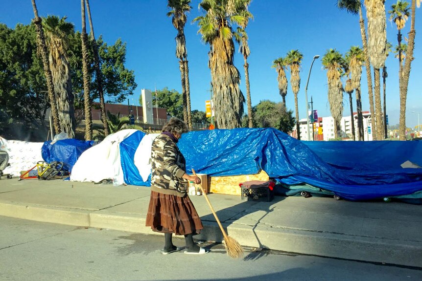 Women sweeps outside an LA tent encampment