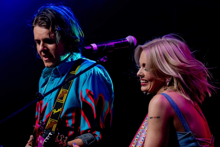 A close up of a man and woman playing their guitars on stage together
