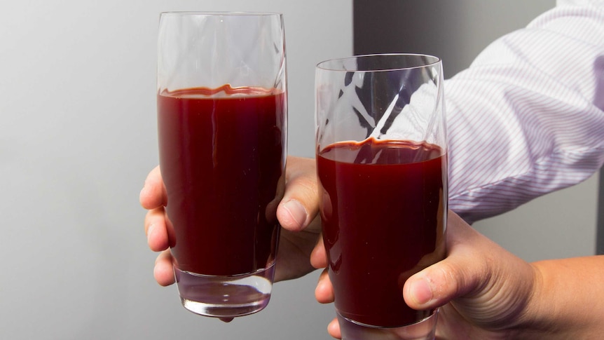 Two hands hold glasses of red beetroot juice.