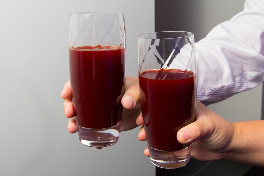 Two hands hold glasses of red beetroot juice.