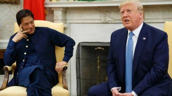 Imran Khan holds his hand up to his face while watching Donald Trump speak at the White House.