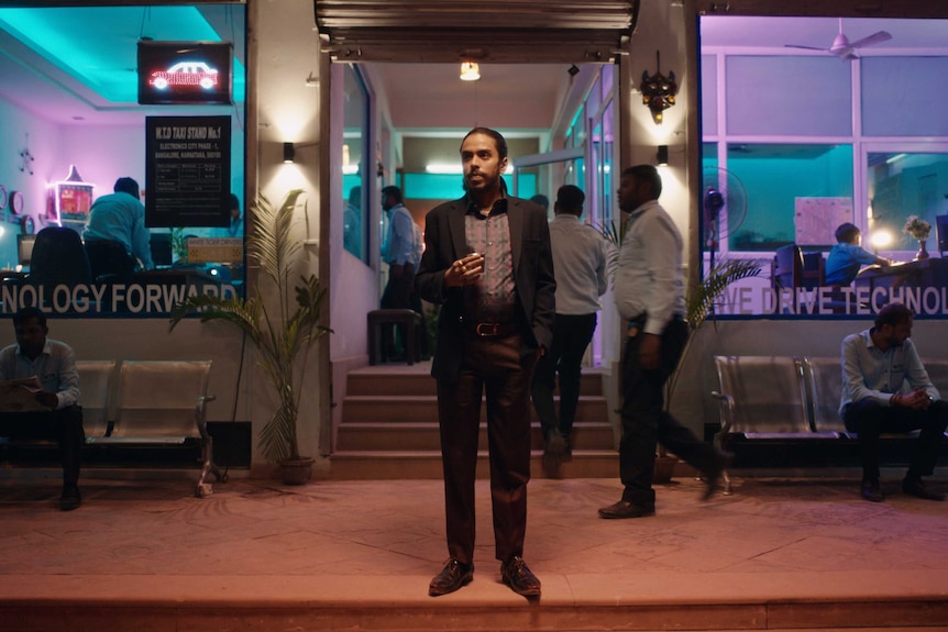 A still from the film The White Tiger with a young man in a suit (Adarsh Gourav) standing in front of a tech business