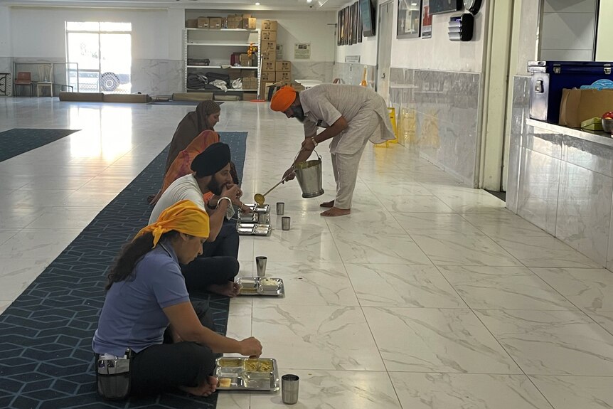 Sikh practitioners gather to receive food on metal trays at the Sikh temple on Logan Road, Queensland.