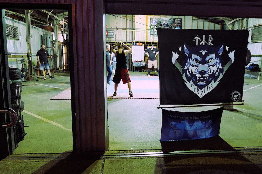 A flag showing a wolf portrait and runic text hangs over a warehouse entrance