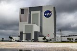 White building with NASA logo on it, dark grey rain clouds in the background.