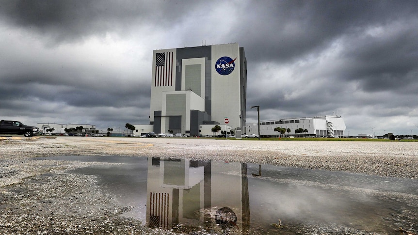 White building with NASA logo on it, dark grey rain clouds in the background.