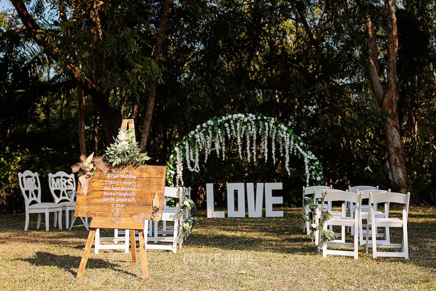 Four chairs on each side of an aisle with a large sign spelling love underneath a leafy, flowery arbor.