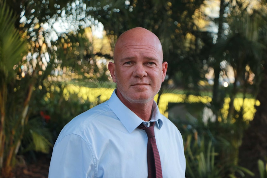 A bald man wearing a pale blue shirt and red tie.