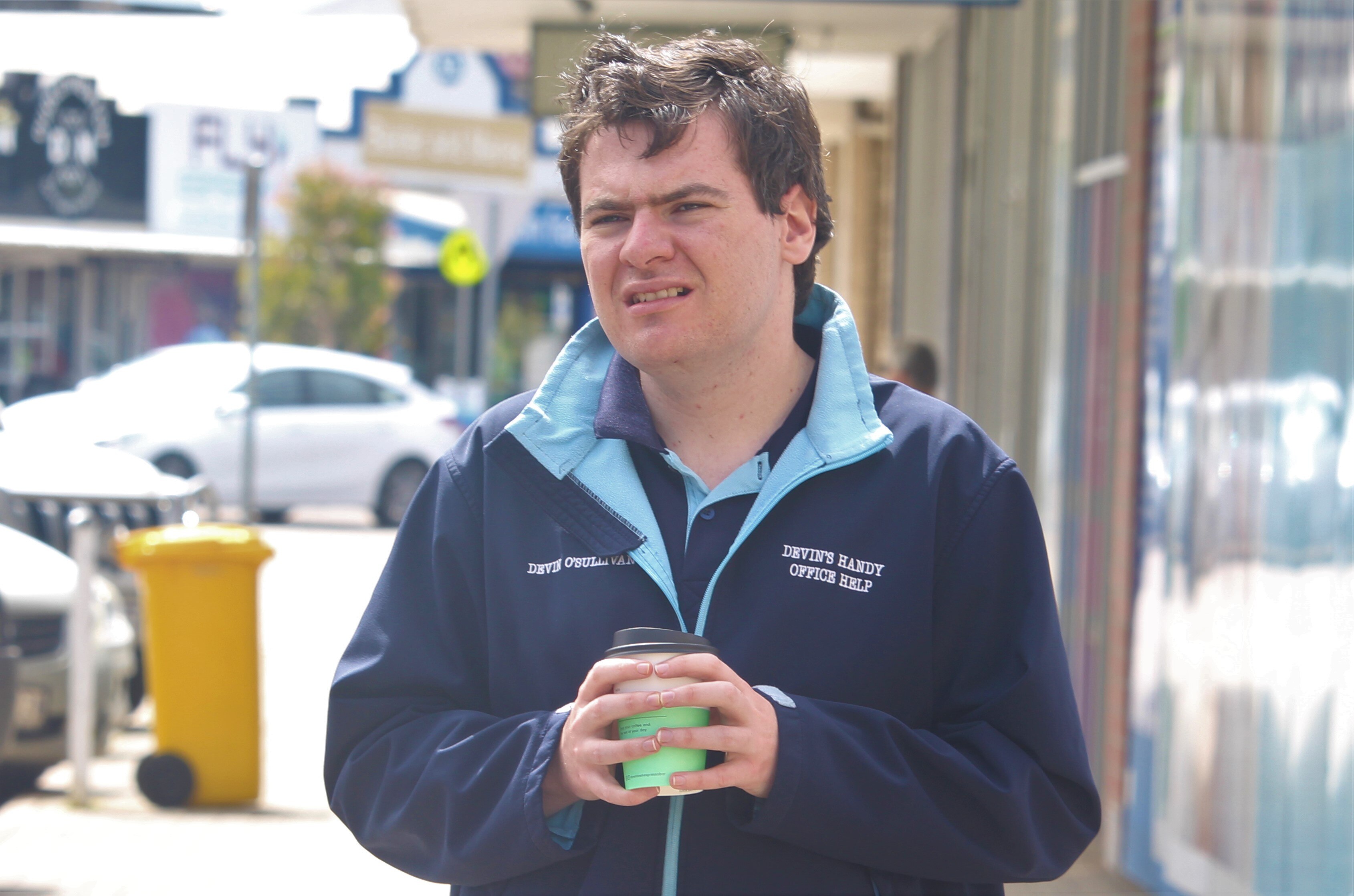 Young man holding a coffee cup and standing in the main street in Esperance