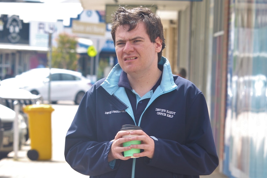 Young man holding a coffee cup and standing in the main street in Esperance