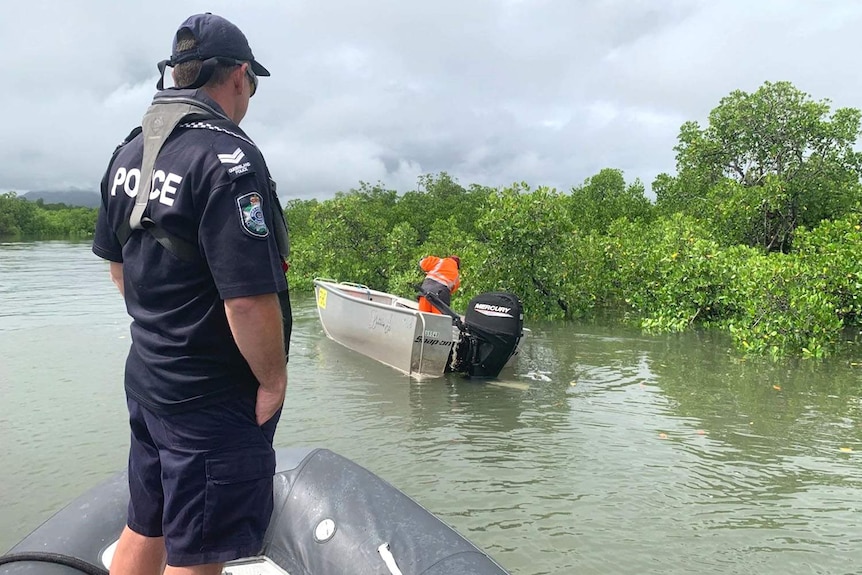 A policeman in an inflatable boat watching someone else searching a nearby dinghy