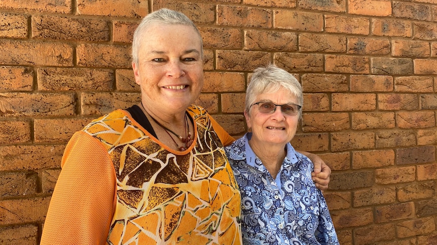 Two grey haired women standing in front of a brick wall.