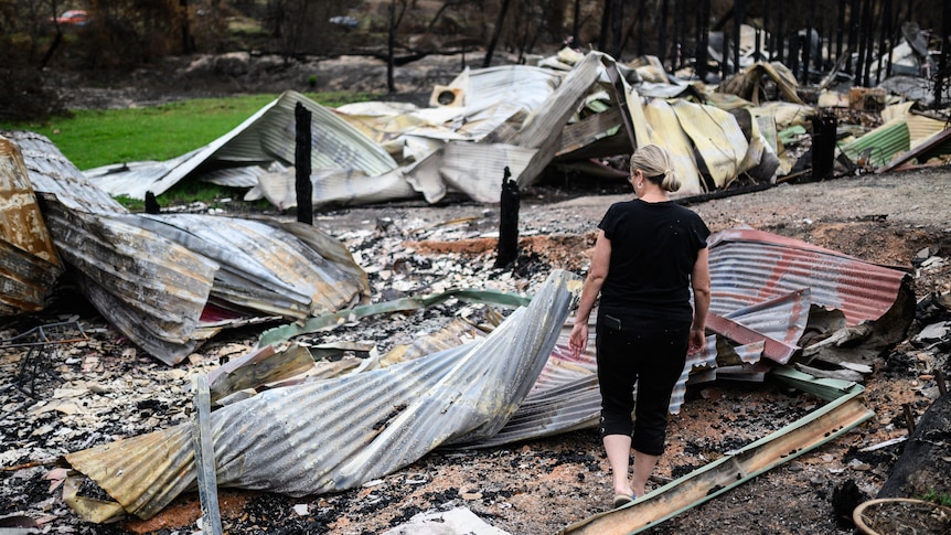 a woman looks at the destruction caused after a bushfire burnt down her home