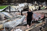 a woman looks at the destruction caused after a bushfire burnt down her home