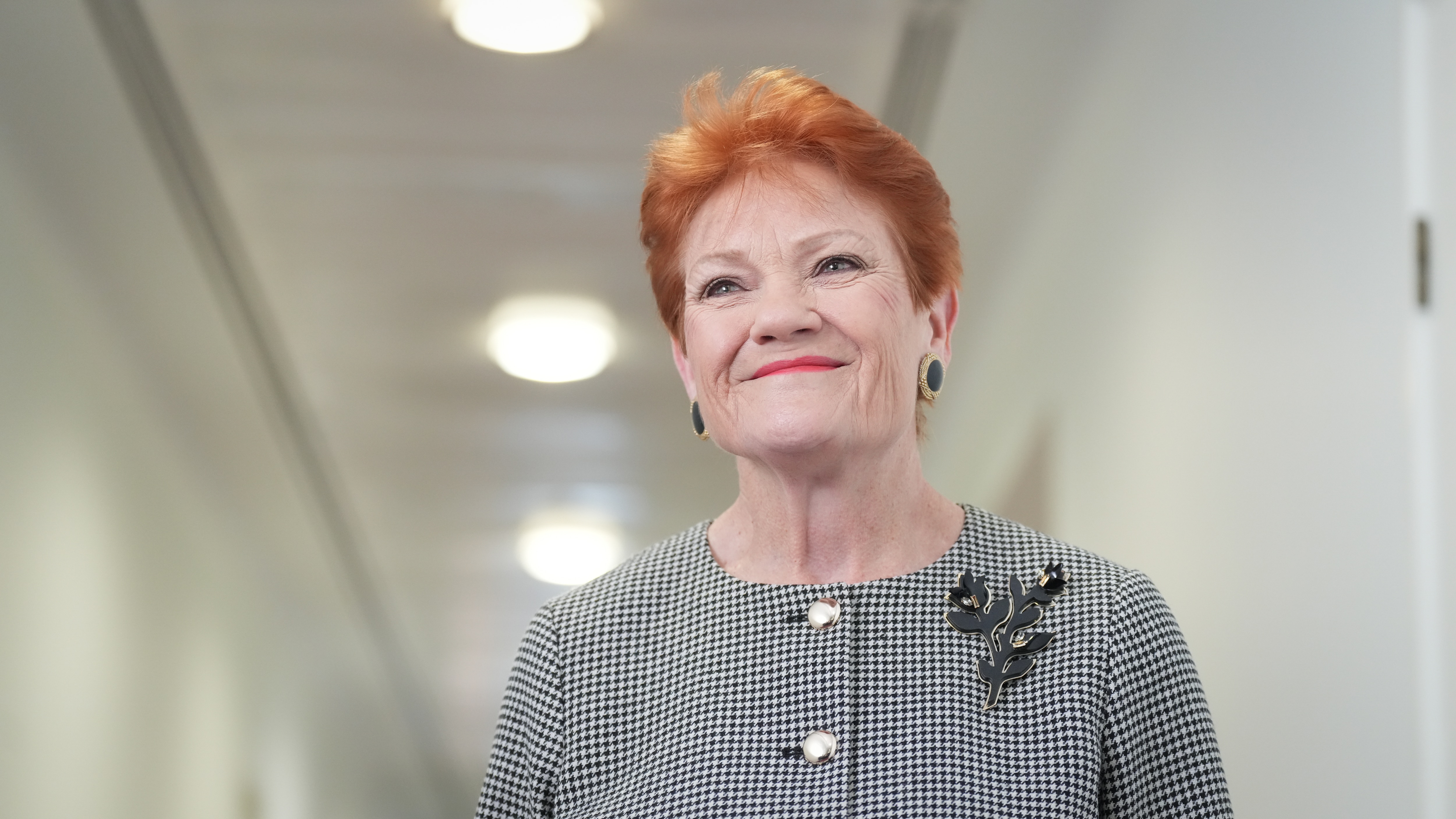 Pauline Hanson stands in a corridor with a smile on her face.