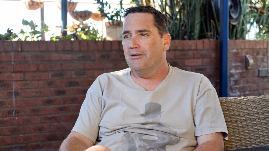 A man wearing a grey t-shirt sits on a chair.