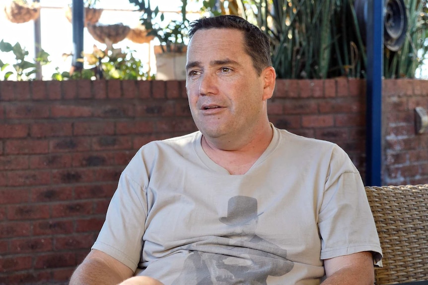 A man wearing a grey t-shirt sits on a chair.