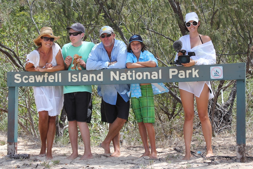 A family of five pose next to a national park sign on a beach
