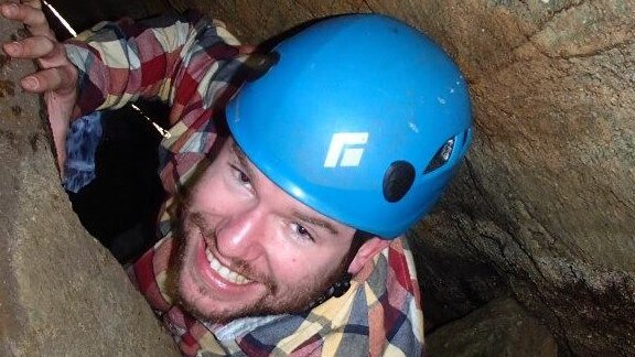 man in cave with helmet, smiling at camera