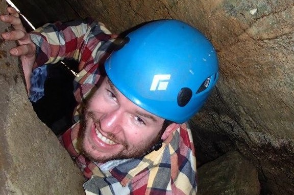 man in cave with helmet, smiling at camera