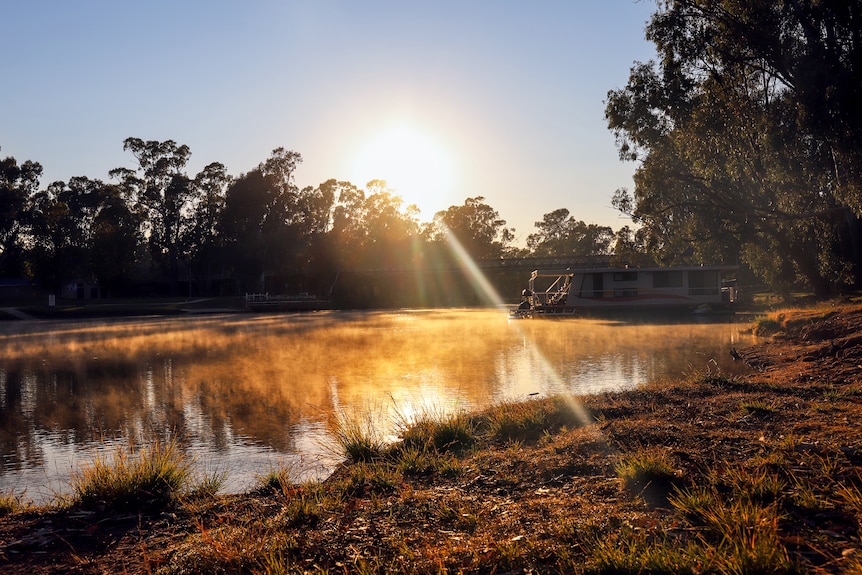 Early morning sunlight hits the Murray river with a bridge and house boat visible in distance