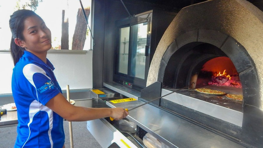 Julia hooks a pizza from inside the oven with a steel utensil.